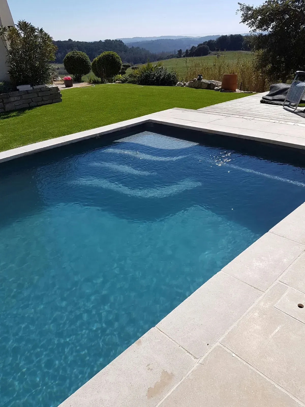 Piscine à l'eau bleue avec escalier, pelouse et collines ondulantes au loin par une journée ensoleillée.