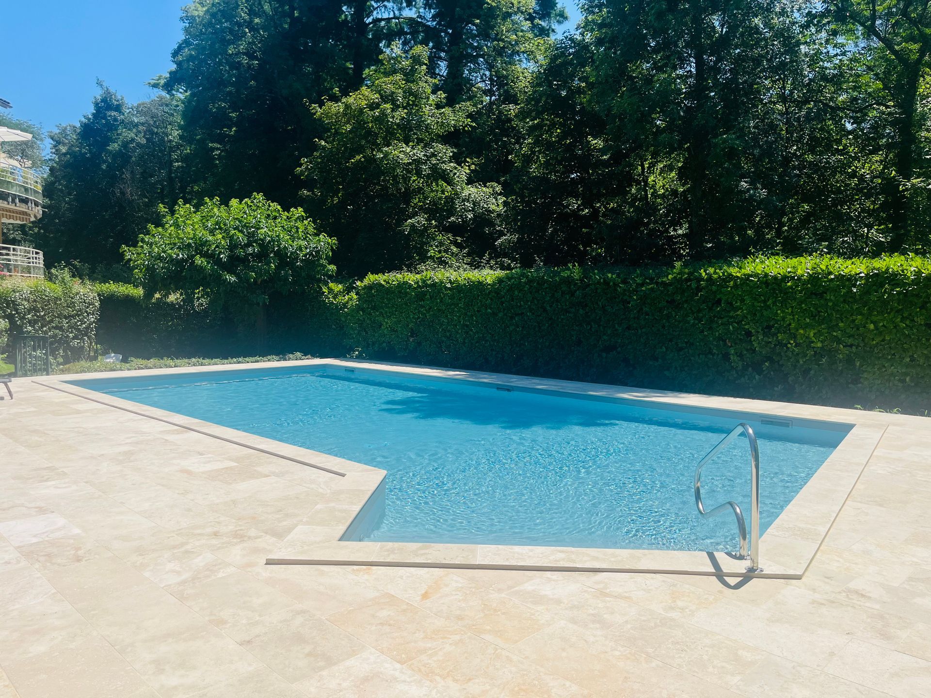 Piscine à l'eau bleue avec terrasse en béton tout autour, et petite aire de jeux aquatiques pour enfants.
