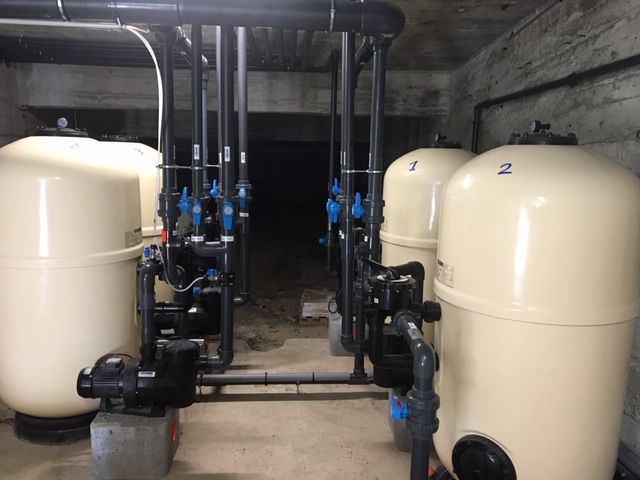 Grands réservoirs de filtration d'eau beiges avec tuyaux noirs et vannes bleues dans une pièce en béton.