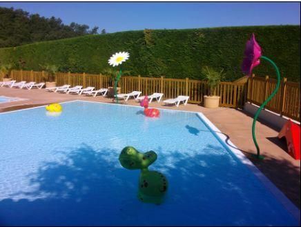 Une piscine avec jeux d'eau, chaises longues et une haie en arrière-plan.