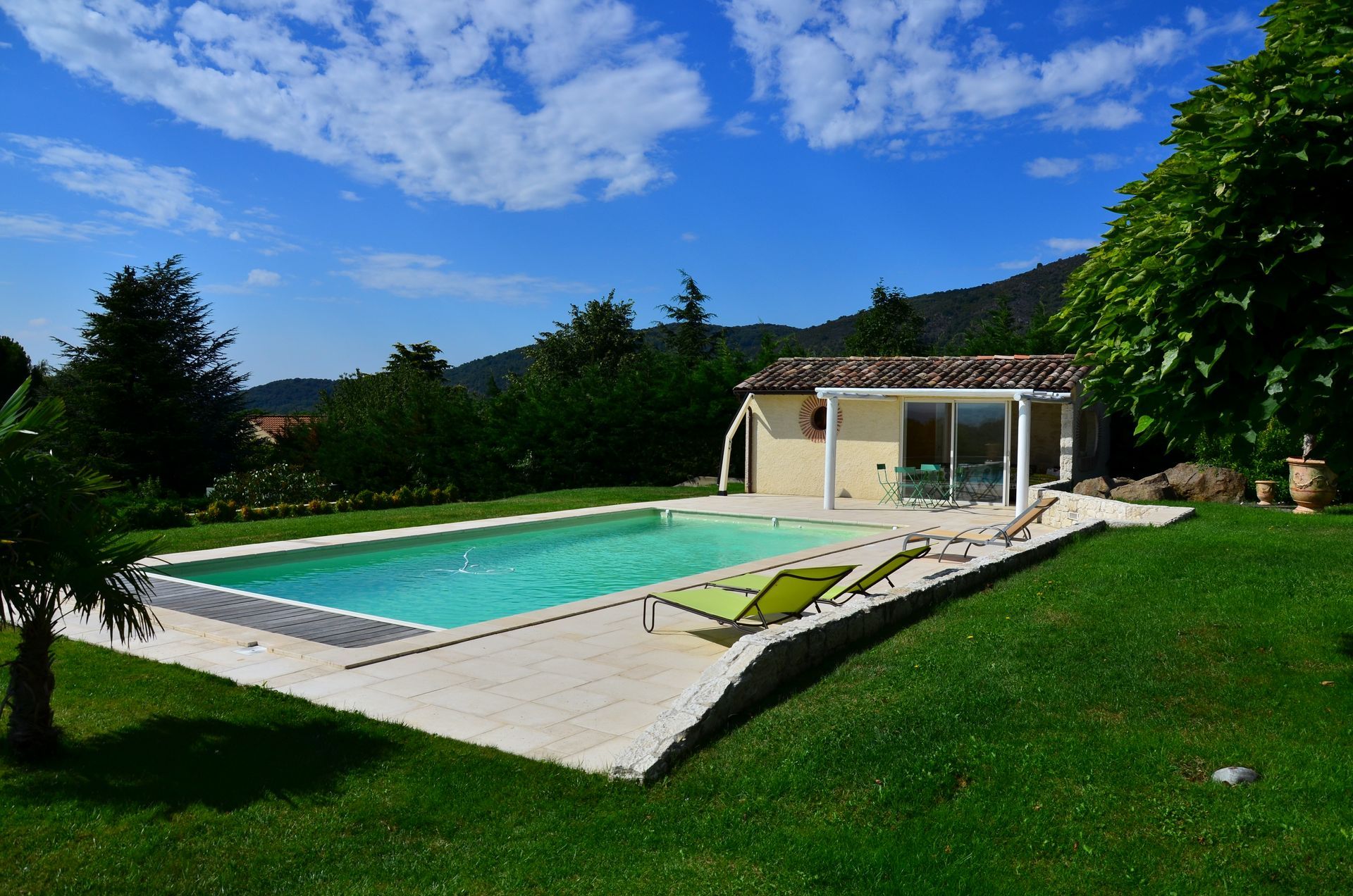 Piscine jouxtant une petite maison avec des chaises longues par une journée ensoleillée.
