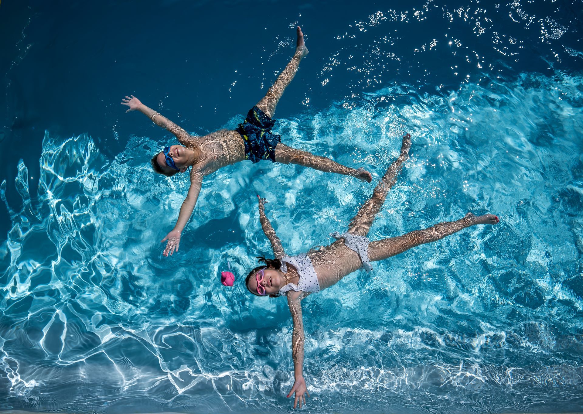 Jardin avec piscine, terrasse en bois, chaises longues, flamant rose gonflable et ciel bleu.