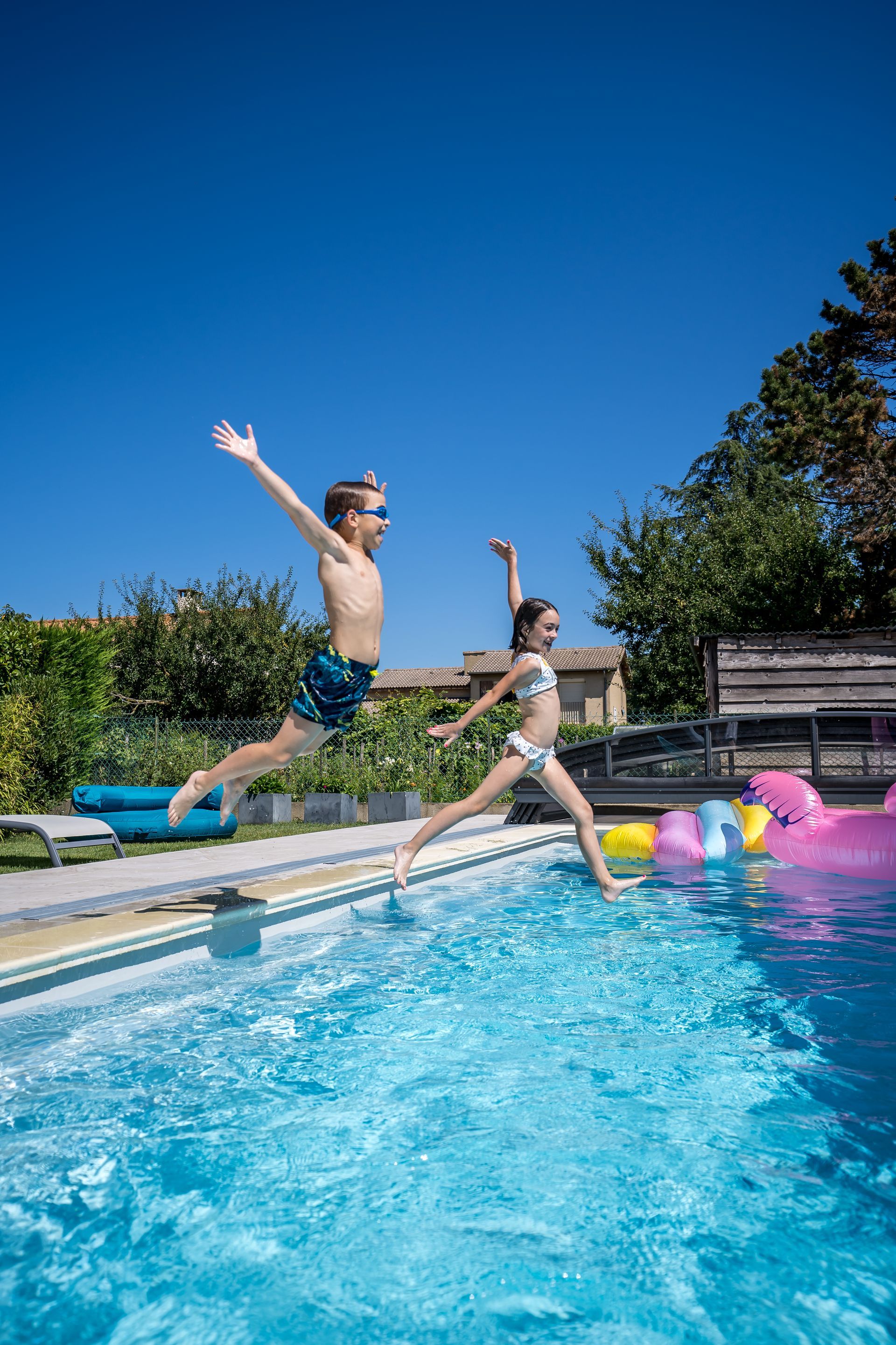 Deux enfants qui sautent dans une piscine par une journée ensoleillée.