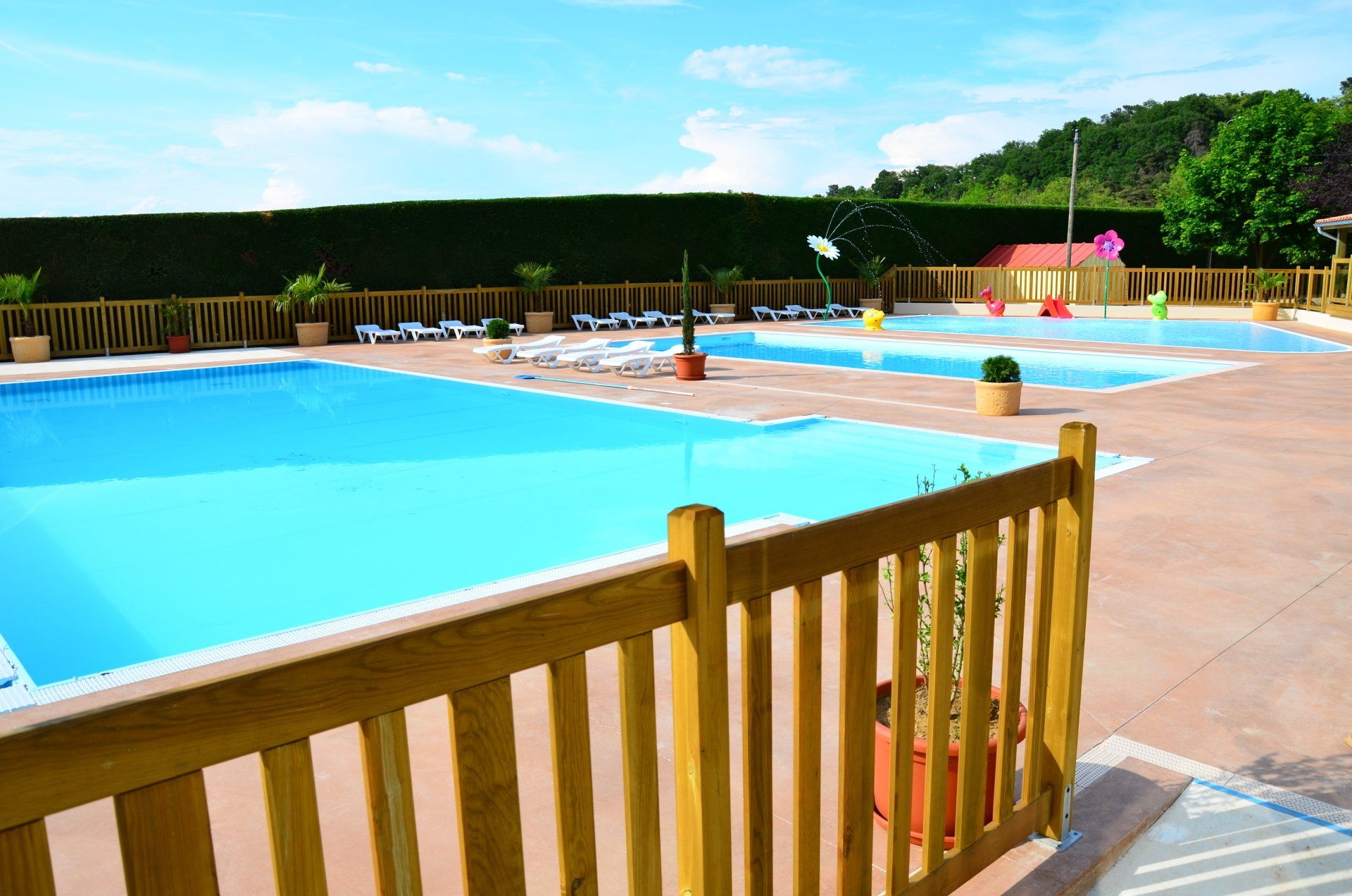 Piscines d'un complexe hôtelier en plein air, entourées de balustrades en bois. Eau bleue, ciel dégagé.