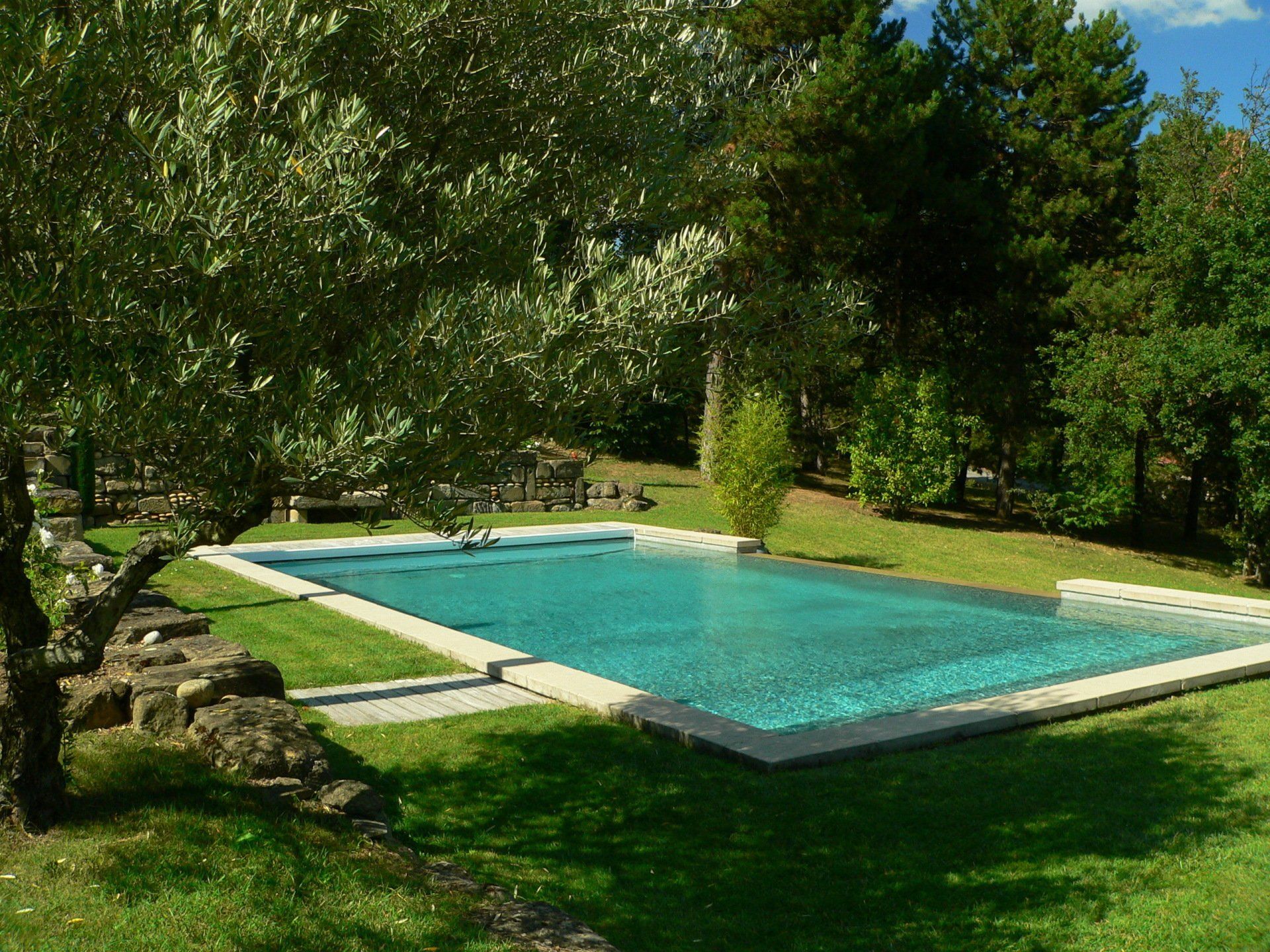 Piscine extérieure rectangulaire entourée de pelouse et d'arbres.