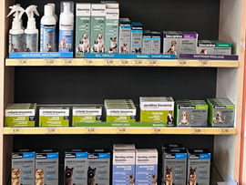 Rayon de vente avec un assortiment de produits de soins pour animaux de compagnie, notamment des sprays, des shampoings et des traitements en boîte dans des emballages bleus, verts et blancs.