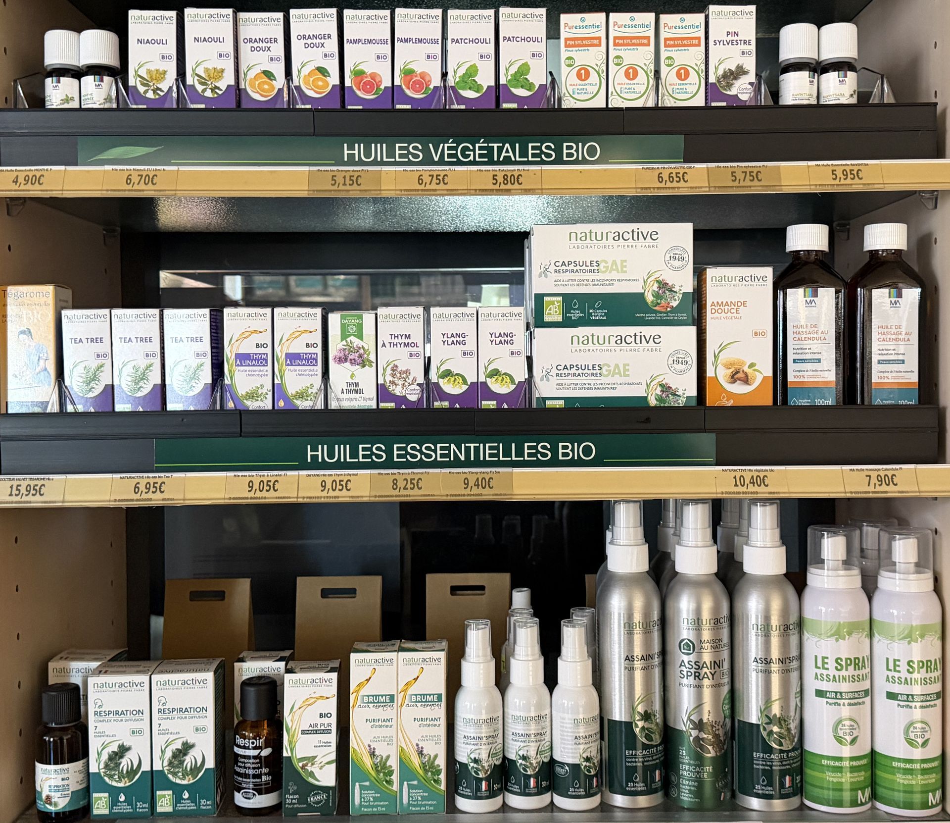Rayonnages d'huiles essentielles et de produits à base de plantes dans un magasin, avec des emballages de couleurs clairs.