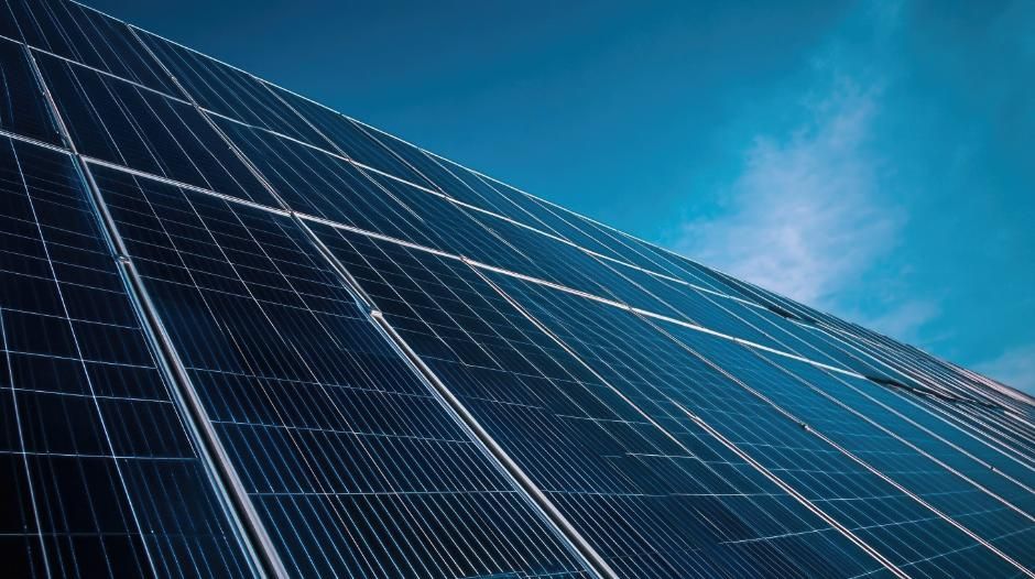 Calentador de agua blanco montado en una pared blanca; la luz del sol proyecta sombras.