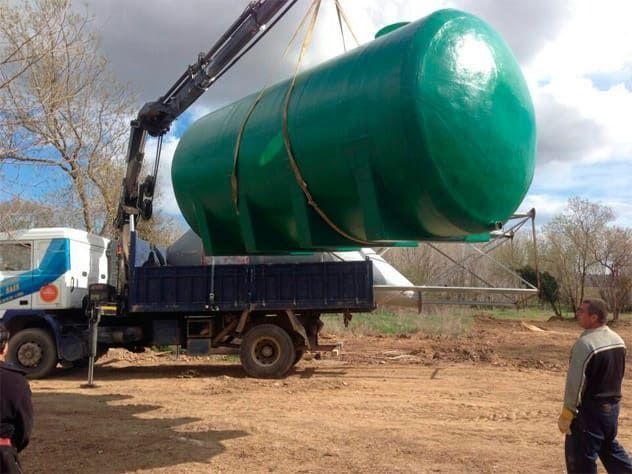 Una grúa sube un gran tanque de agua verde a la caja de un camión. Dos hombres están cerca.