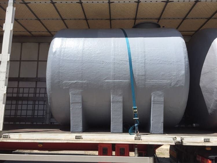 Tanque grande de color gris asegurado con una correa azul dentro de la caja de una camioneta.