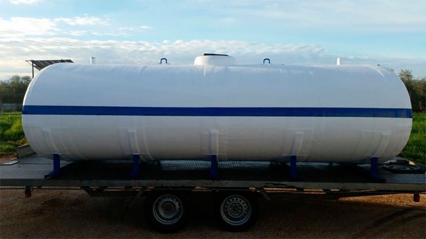 Tanque cilíndrico blanco con franja azul sobre remolque, al aire libre.