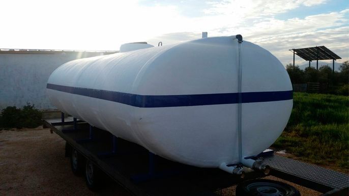 Tanque de agua blanca en un remolque, franja azul, entorno al aire libre.