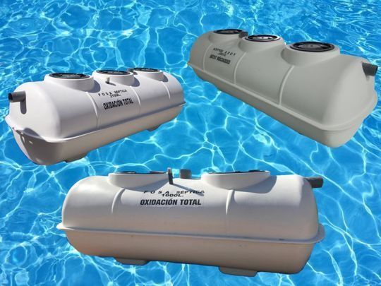 Tres fosas sépticas blancas sobre fondo de agua azul. Cada una tiene dos o tres tapas de acceso circulares.