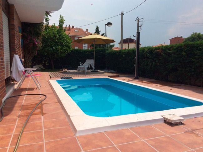 Piscina en el patio trasero con agua turquesa, rodeada de azulejos rojos y molduras blancas, con una sombrilla amarilla.