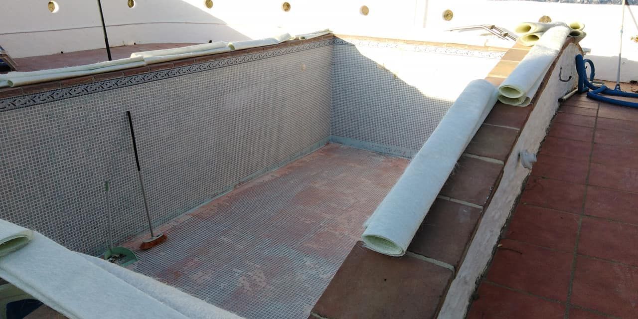 Una piscina vacía con una capa protectora en proceso de instalación. Rollos de material blanco descansan sobre el borde de ladrillo.