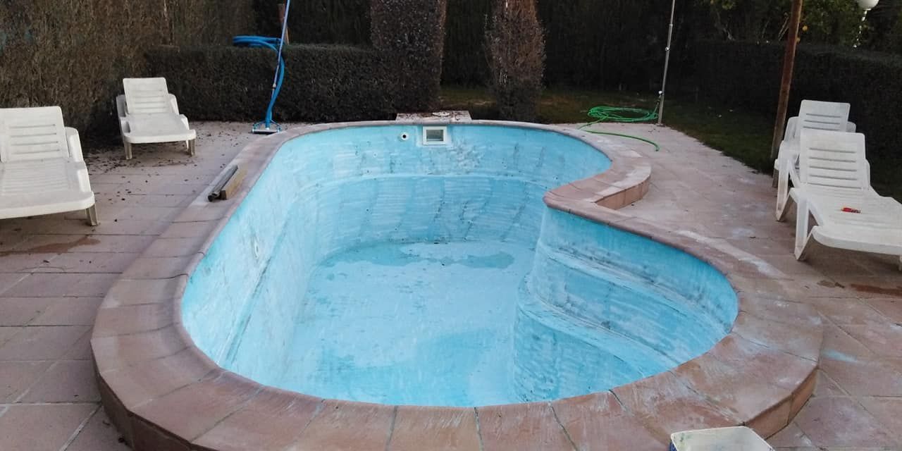 Una piscina vacía, con forma de corazón y azulejos azules, rodeada por una terraza de piedra y tumbonas.
