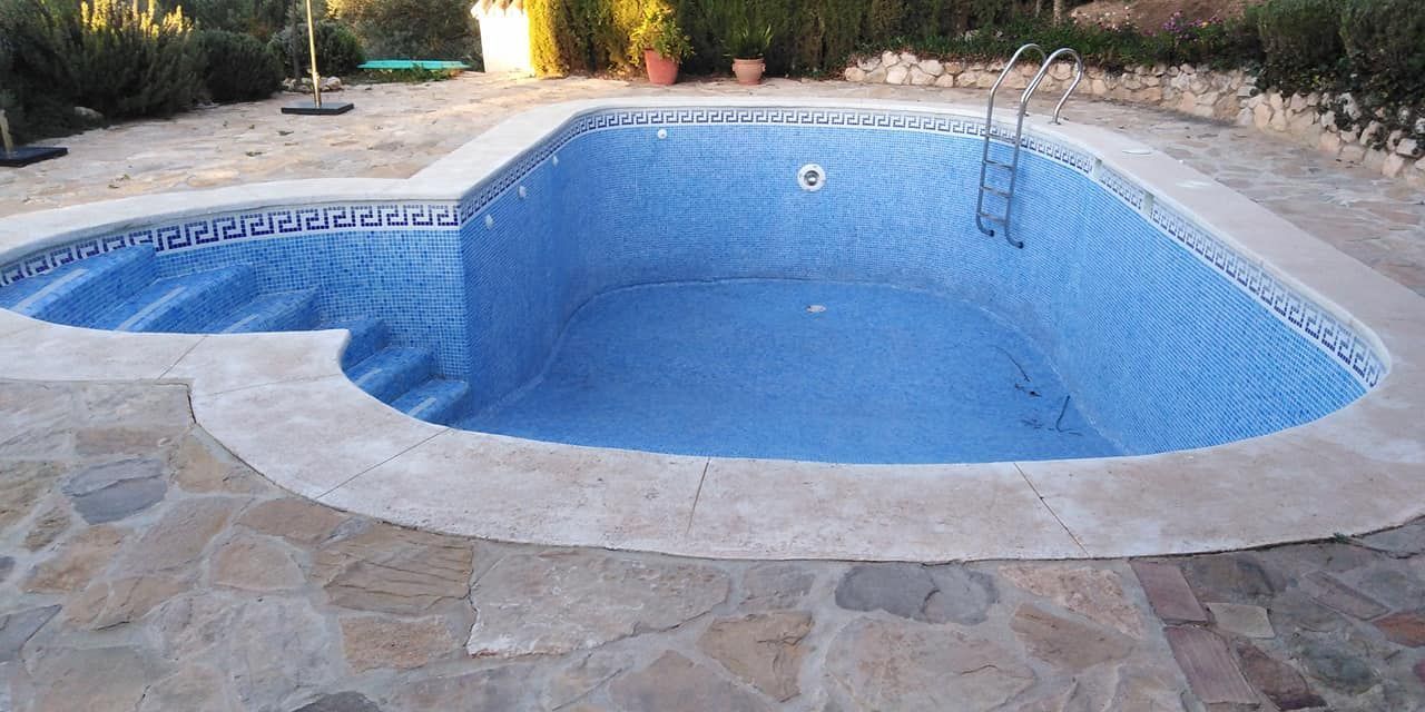 Piscina vacía de azulejos azules rodeada de un patio de piedra, con escalones y escalera.