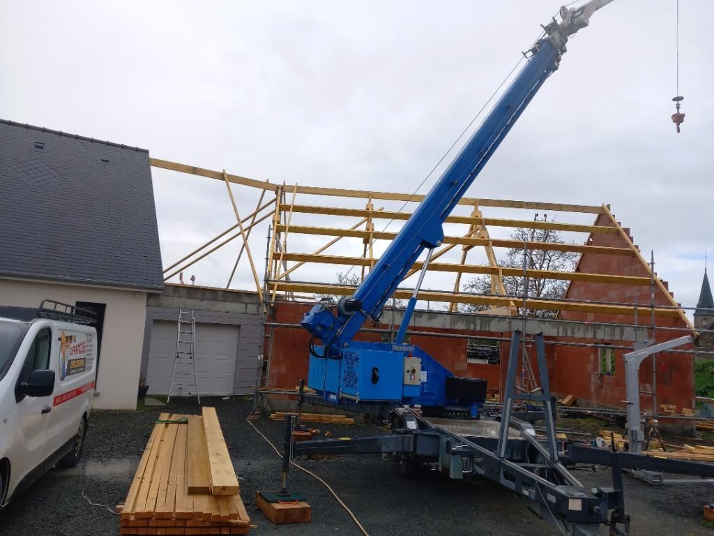 Une grue bleue soulève des poutres en bois pour les poser sur un bâtiment en briques en construction.