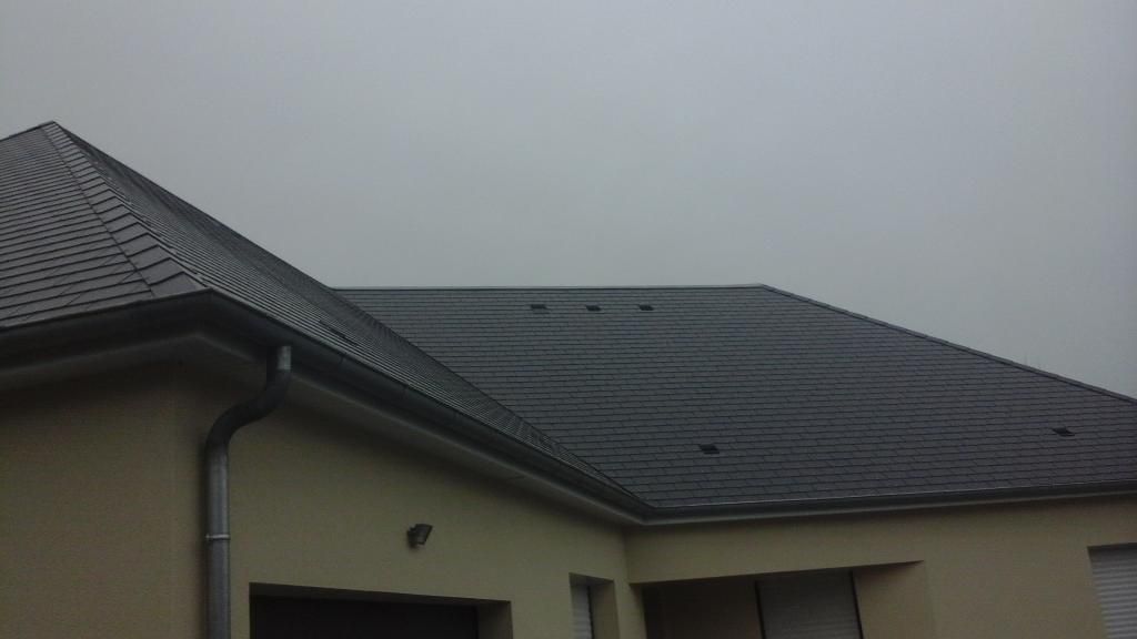 Maison beige avec toit de tuiles grises et ciel gris.