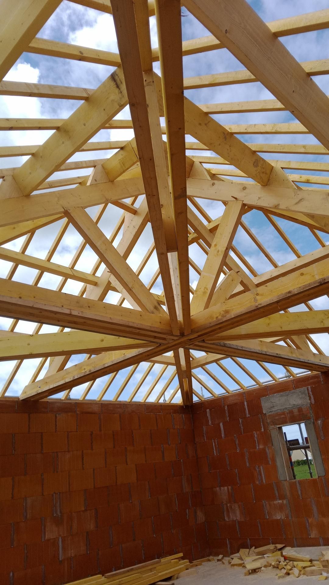Charpente en bois en construction au-dessus d'un mur de briques. Lumière du jour vive visible à travers la structure.