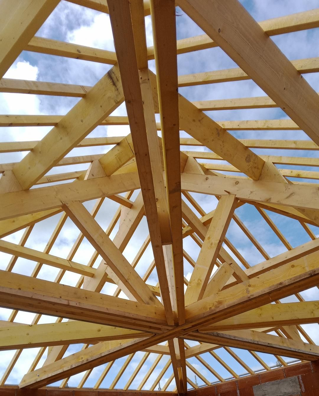 Charpente de toit en bois en construction, ciel bleu visible.