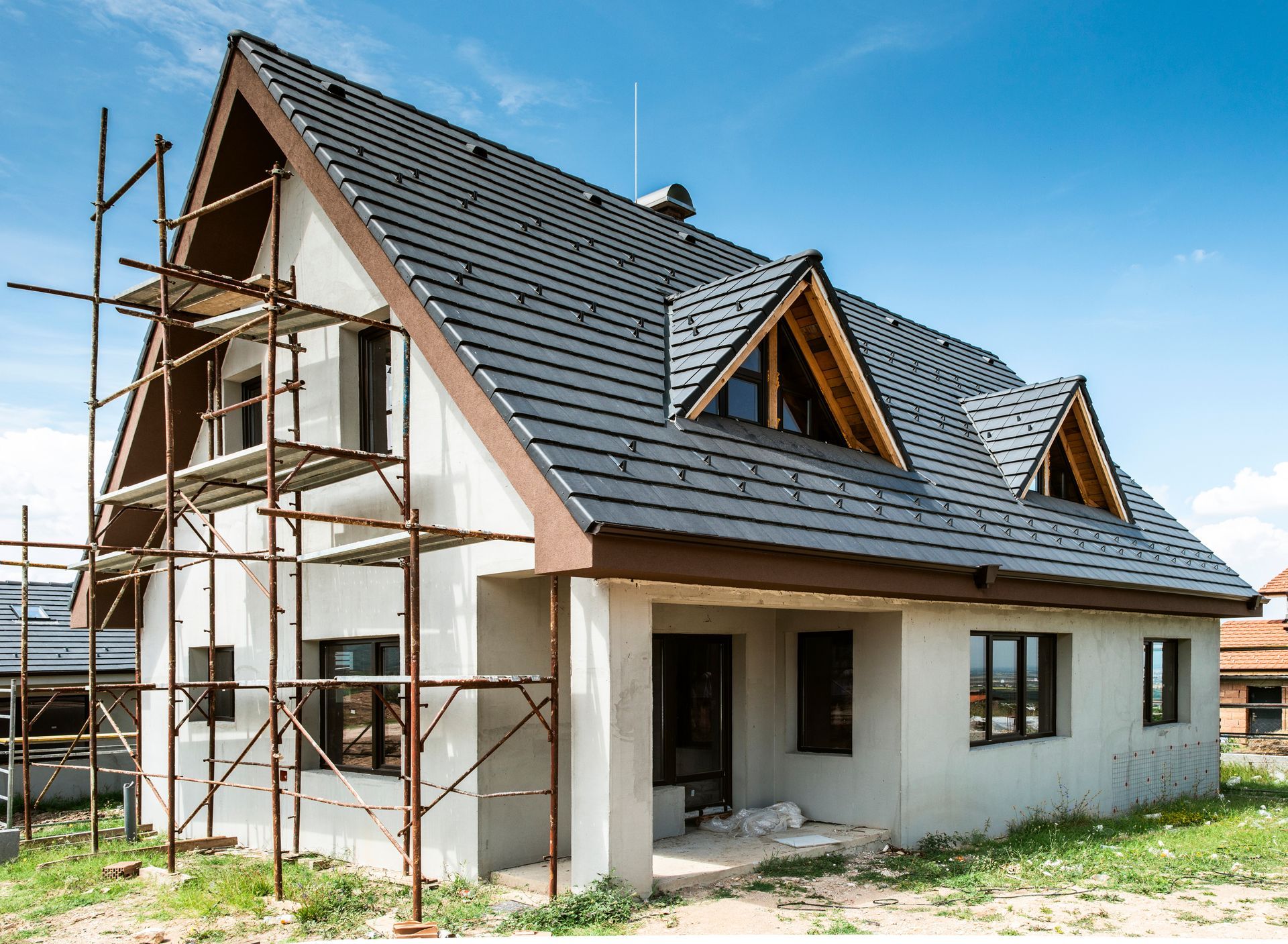 Maison en construction avec échafaudages et toit gris foncé.