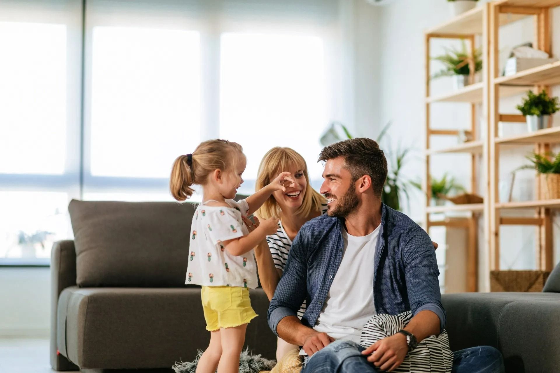 Une famille assise sur un canapé dans un salon lumineux, souriant et interagissant avec un jeune enfant.