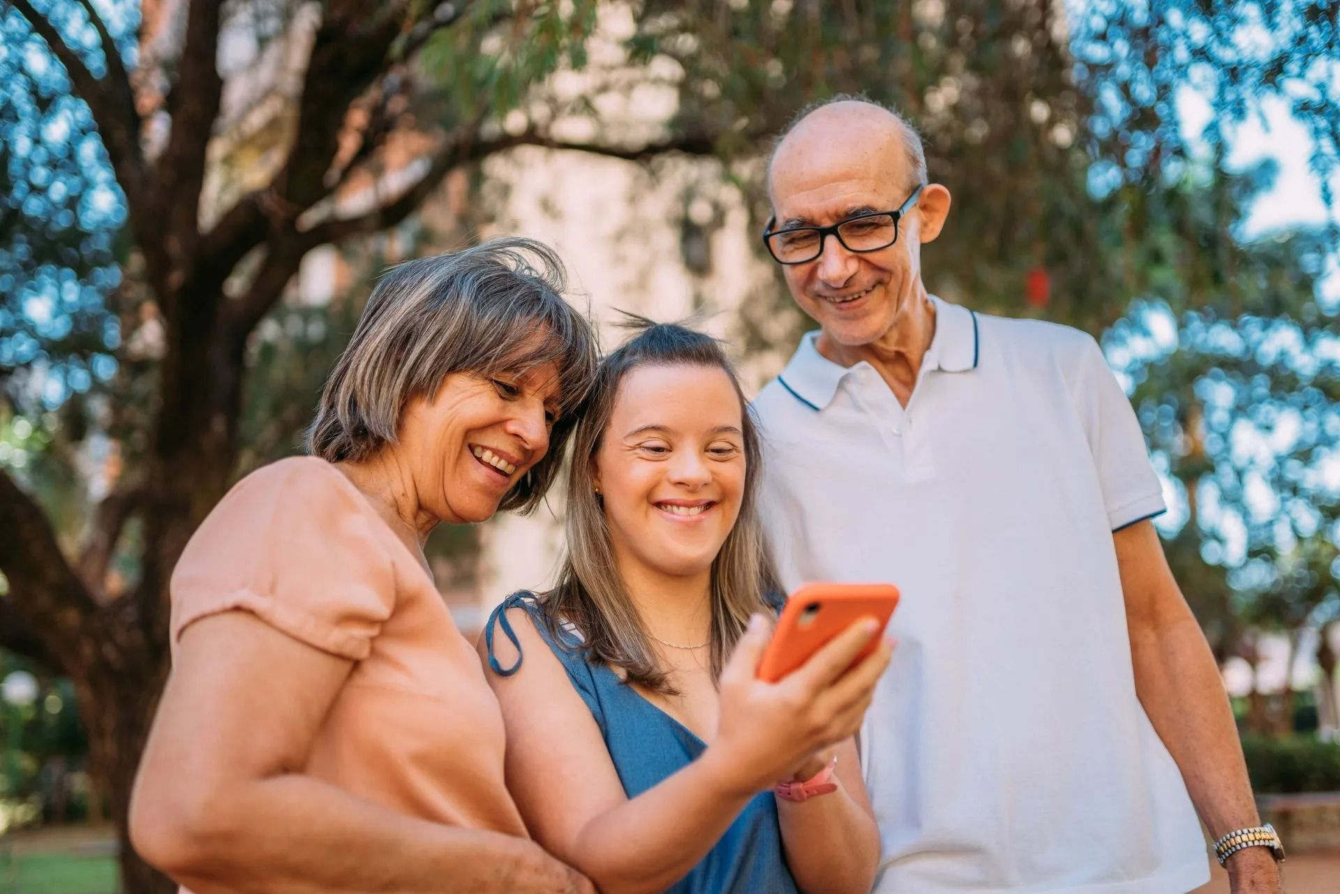 Trois personnes sourient à l'extérieur en regardant un téléphone.