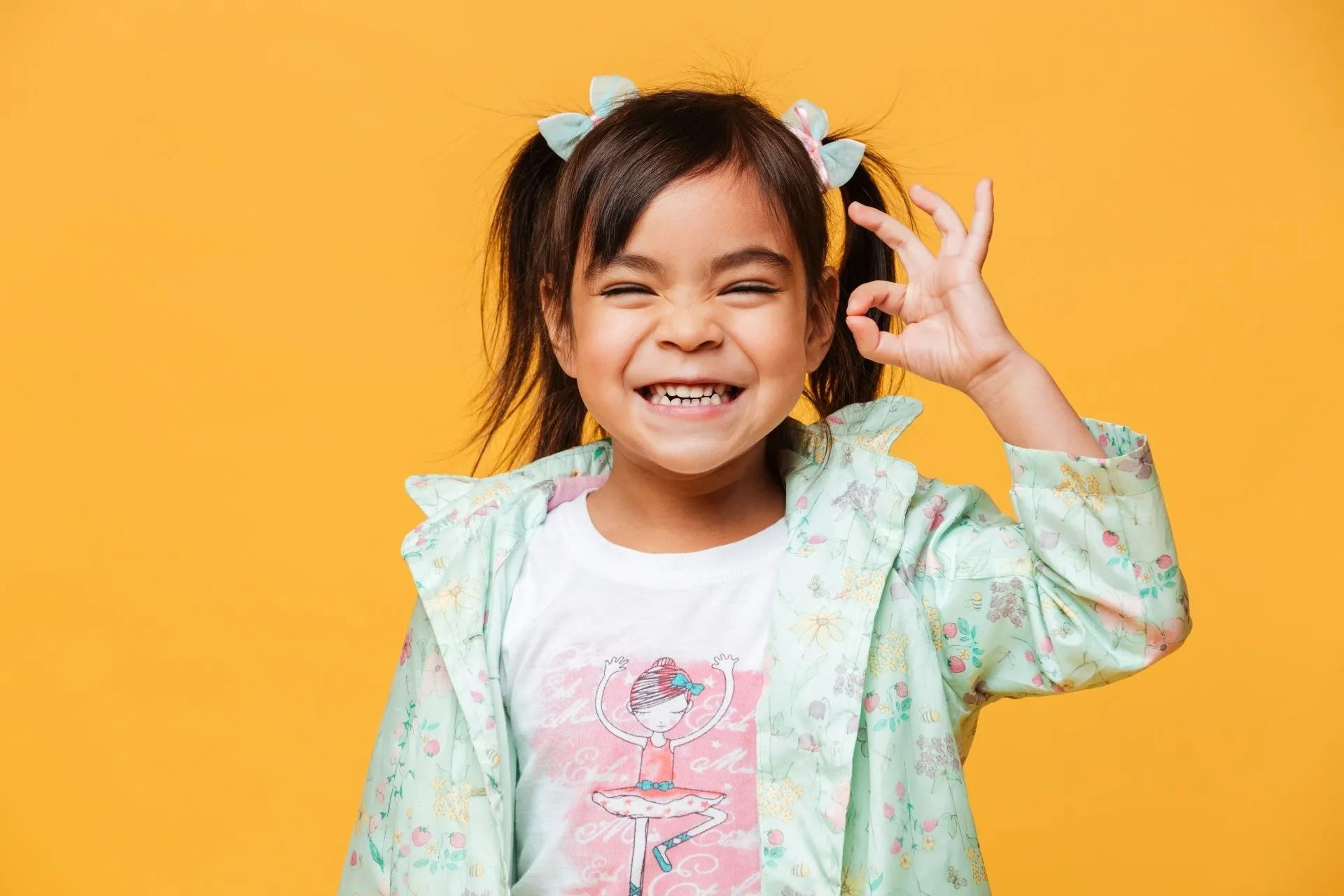 Enfant souriant faisant le signe OK avec la main sur un fond orange vif.