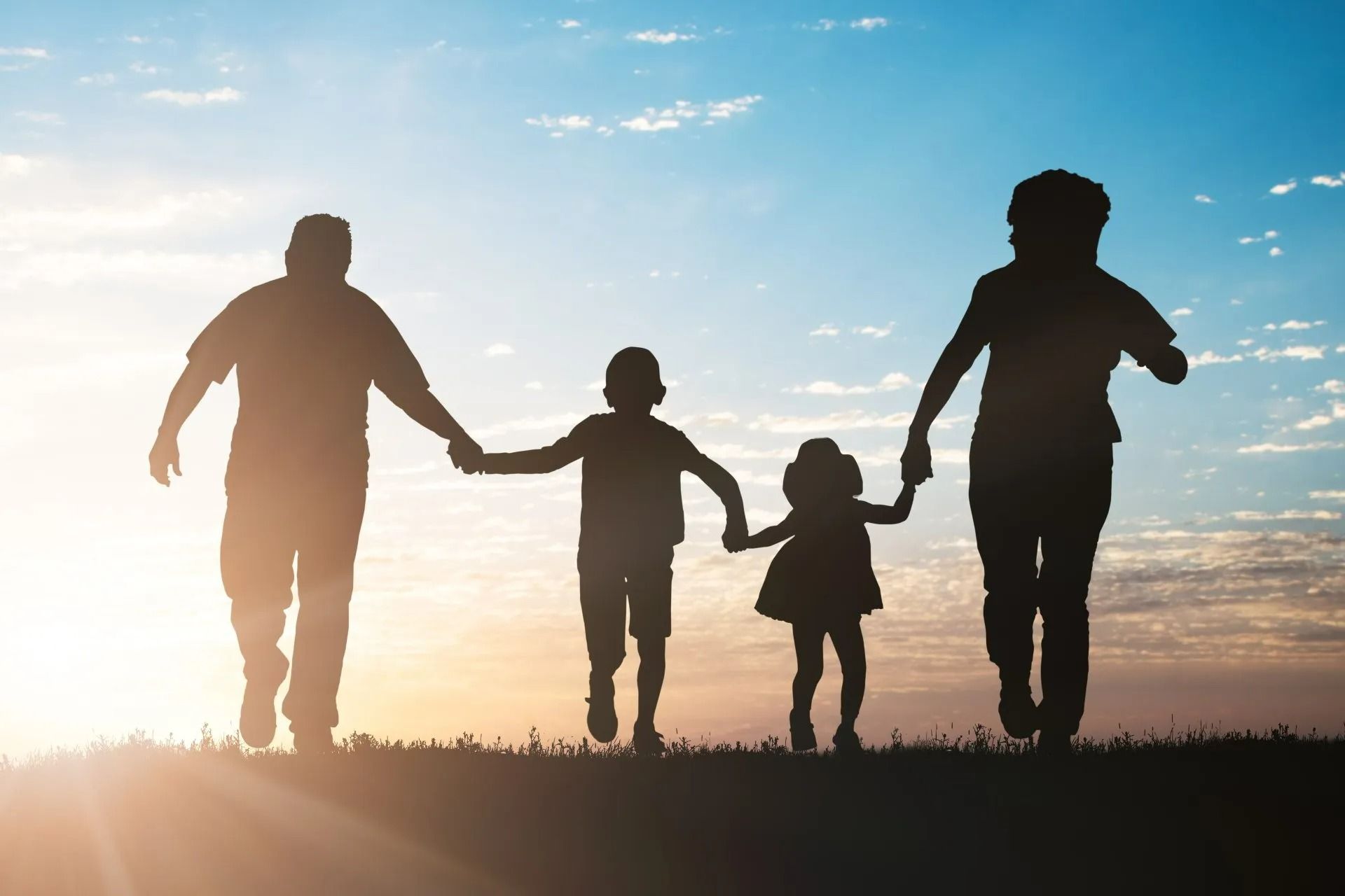 Une famille de quatre personnes se tient la main et se promène au coucher du soleil.