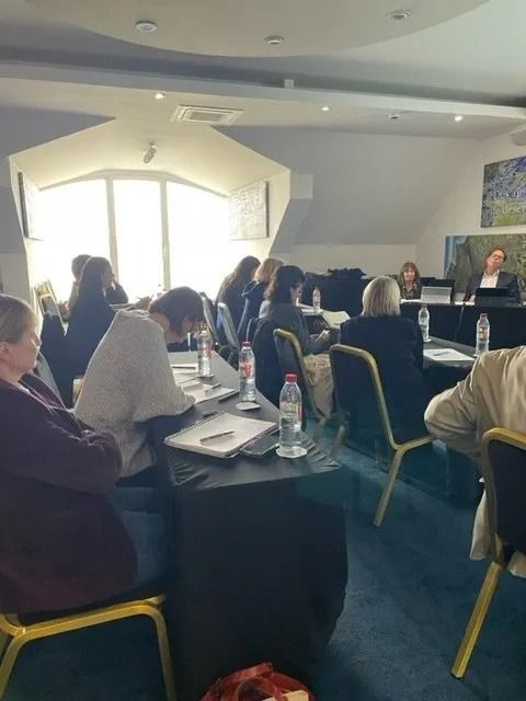 Des participants à une formation, assis à des tables dans une salle de conférences lumineuse, écoutent un orateur au premier rang.