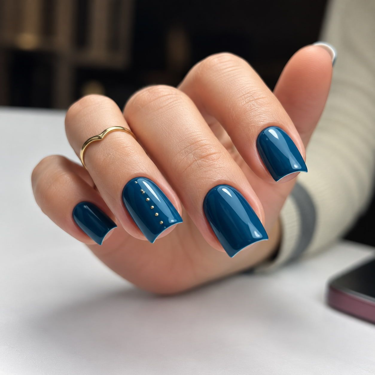 Mano con esmalte de uñas azul brillante y un anillo fino de oro apoyada sobre una mesa
