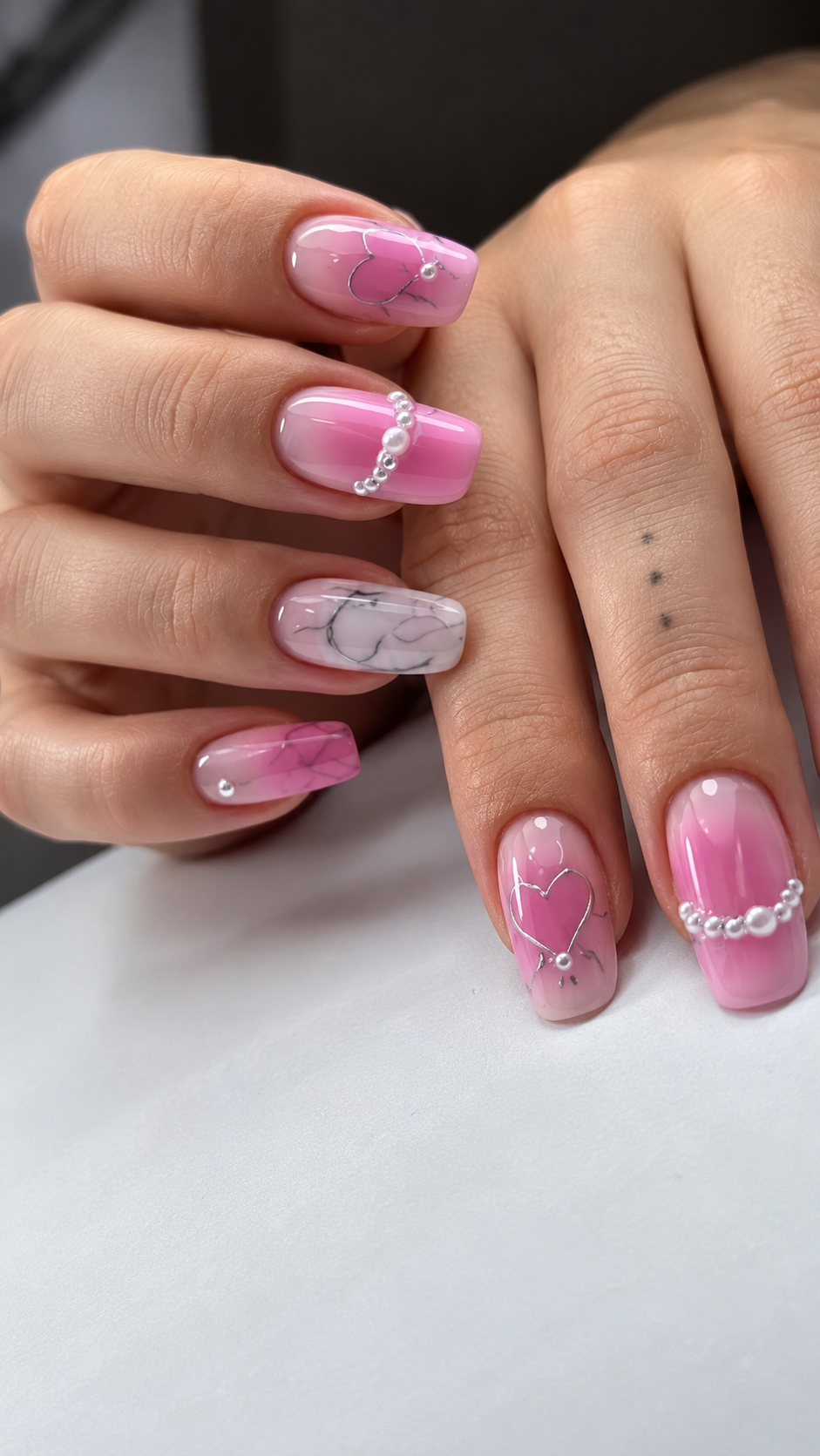 Manos con uñas decoradas con motivos florales en rosa y blanco, y una uña de acento con un diseño de corazón.