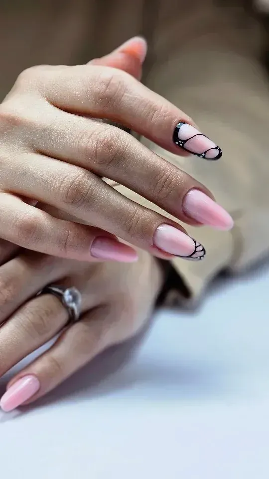 Manos con las uñas rosas y diseños florales negros, apoyadas juntas sobre una superficie blanca.