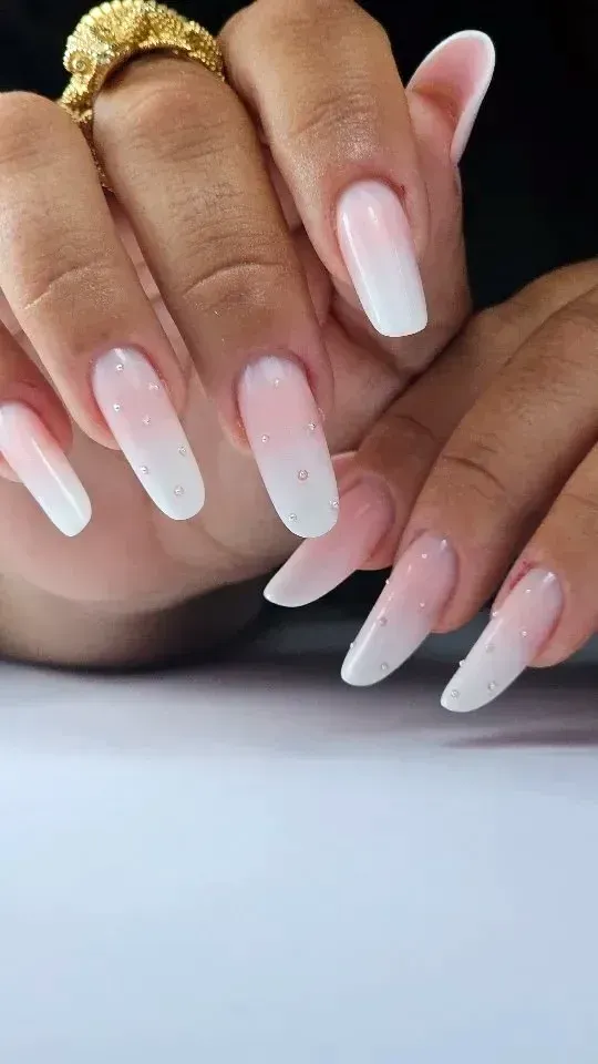 Primer plano de unas manos con uñas acrílicas largas con efecto degradado blanco y un anillo dorado