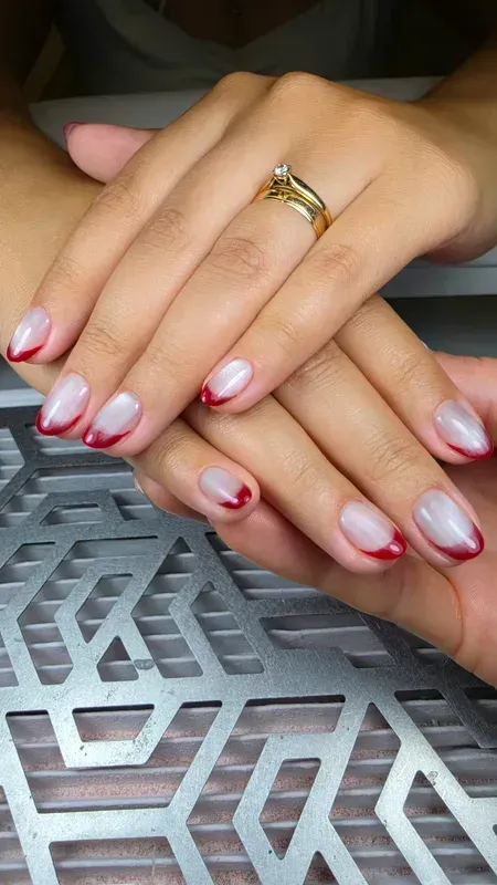 Manos con uñas cuidadas en tonos rosa y blanco apoyadas sobre una mesa metálica estampada.
