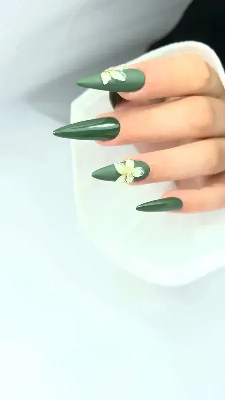 Mano con uñas largas cuidadas de color verde salvia y un pequeño detalle floral blanco en un dedo