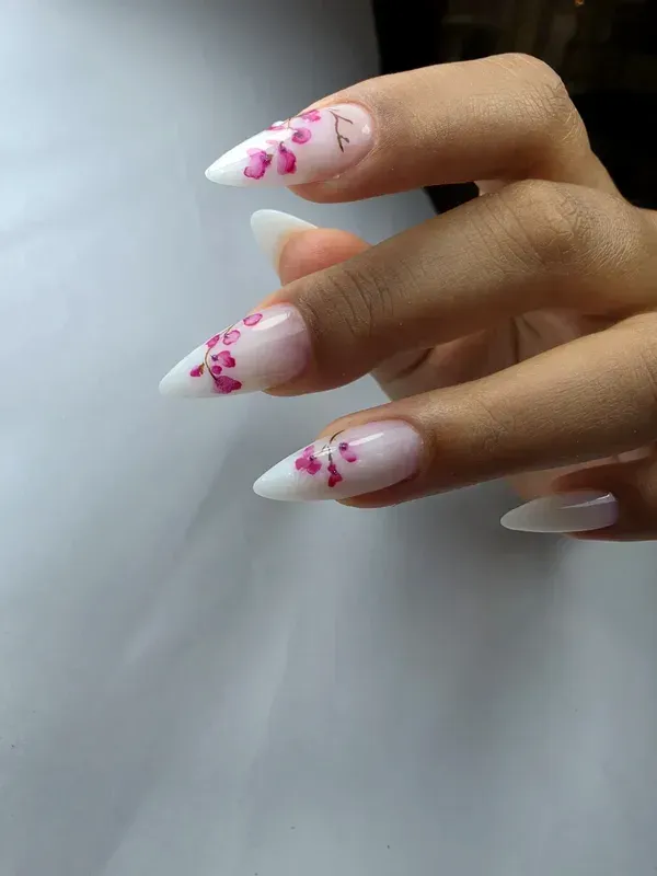 Mano con uñas largas blancas y las puntas decoradas con motivos florales rosas sobre un fondo claro
