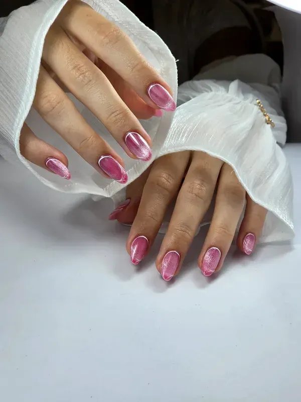 Manos con uñas cuidadas de color rosa brillante apoyadas sobre una tela blanca
