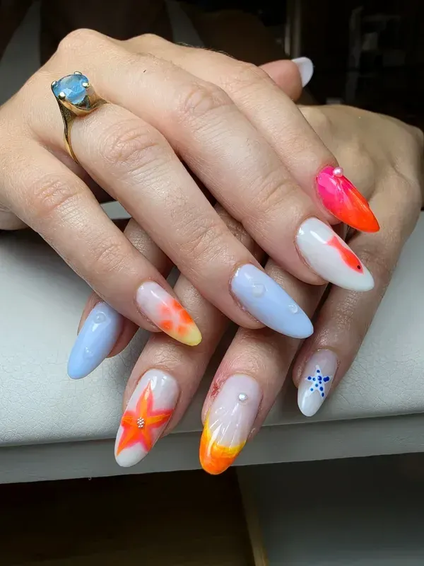 Manos con uñas largas y coloridas y un anillo con una gema azul apoyadas sobre una superficie clara