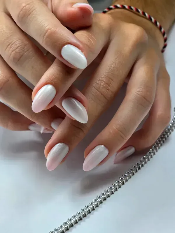 Manos con las uñas arregladas en rosa pálido y una pulsera apoyadas sobre una superficie blanca