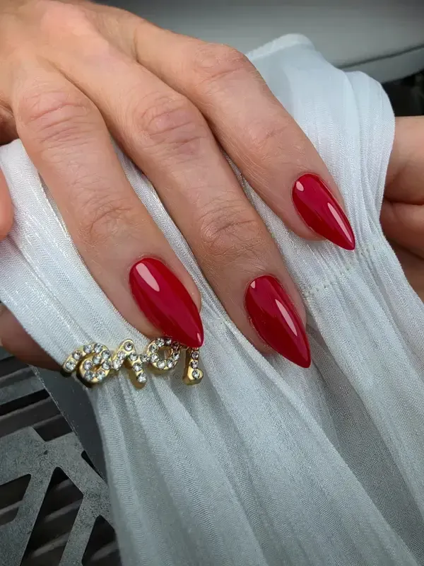 Mano con uñas largas y rojas, cuidadas, apoyada sobre una tela blanca y con un anillo de oro con piedras transparentes