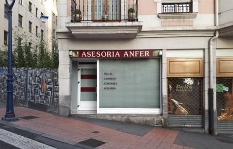 Vista a pie de calle de la fachada de la oficina de Asesoría Anfer, con letrero rojo y ventana de cristal.