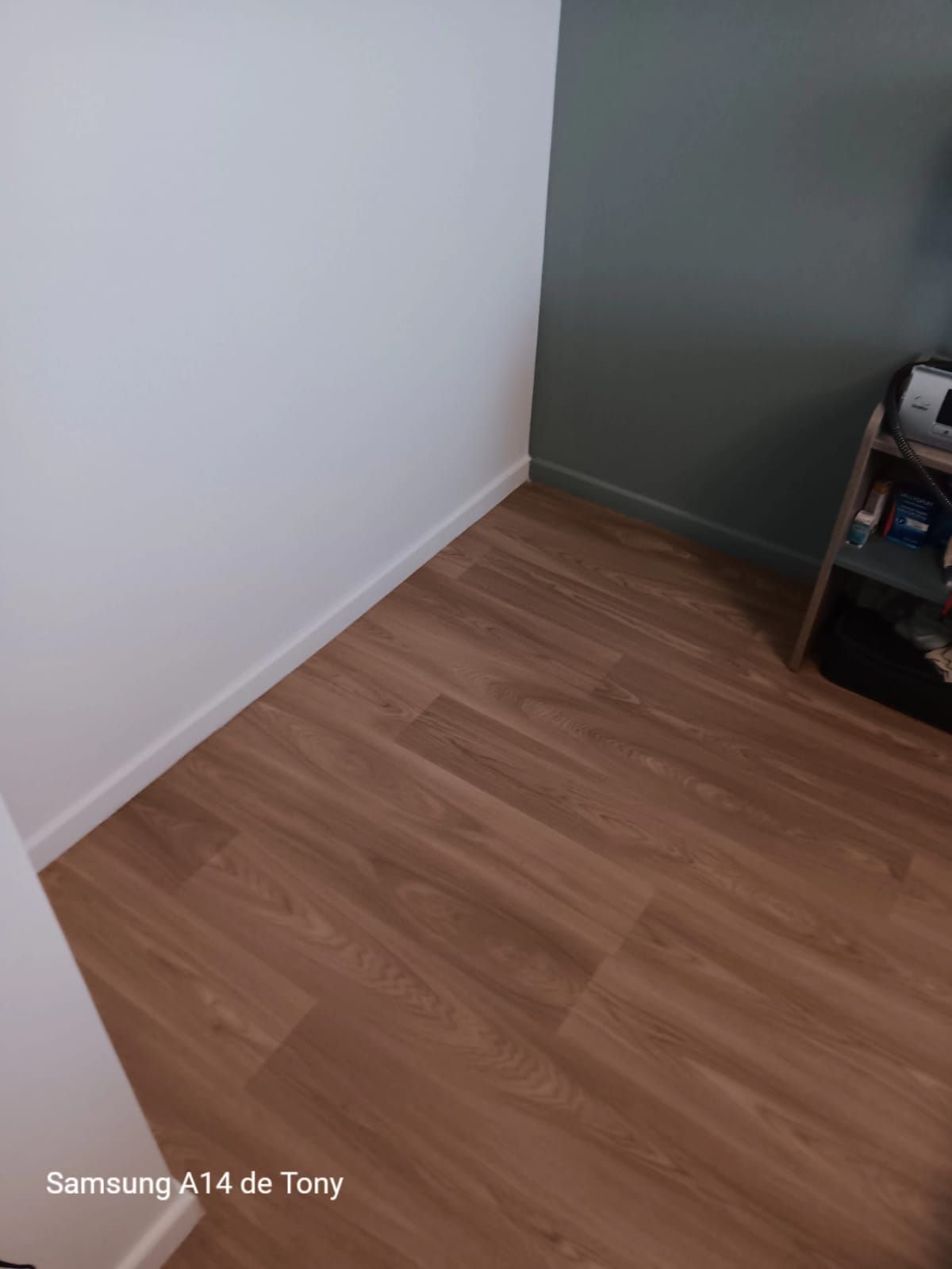 Un coin de pièce avec un parquet clair à motifs, un mur blanc, un mur gris foncé et des plinthes blanches.