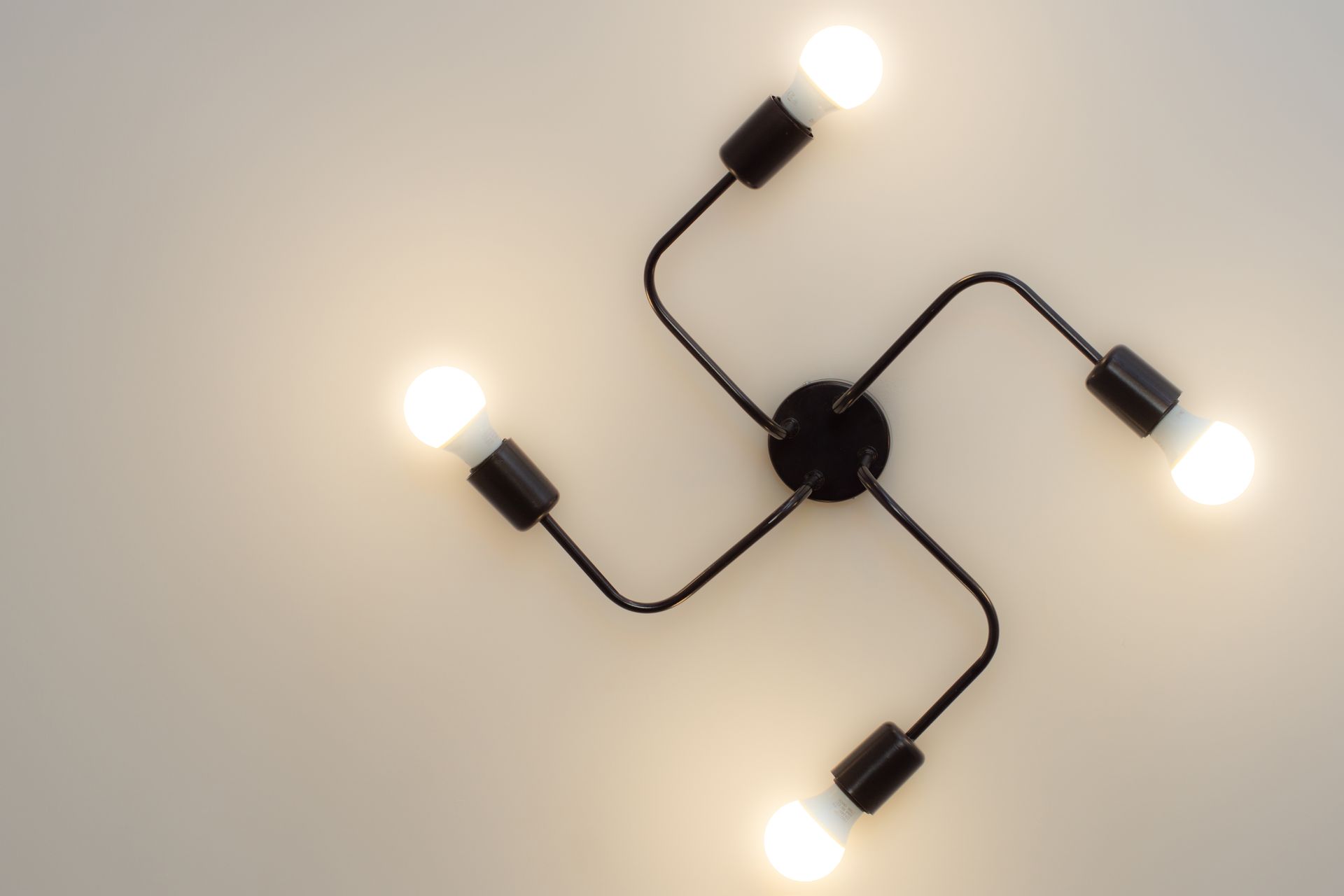 Plafonnier avec quatre ampoules lumineuses et bras incurvés noirs sur un plafond beige.