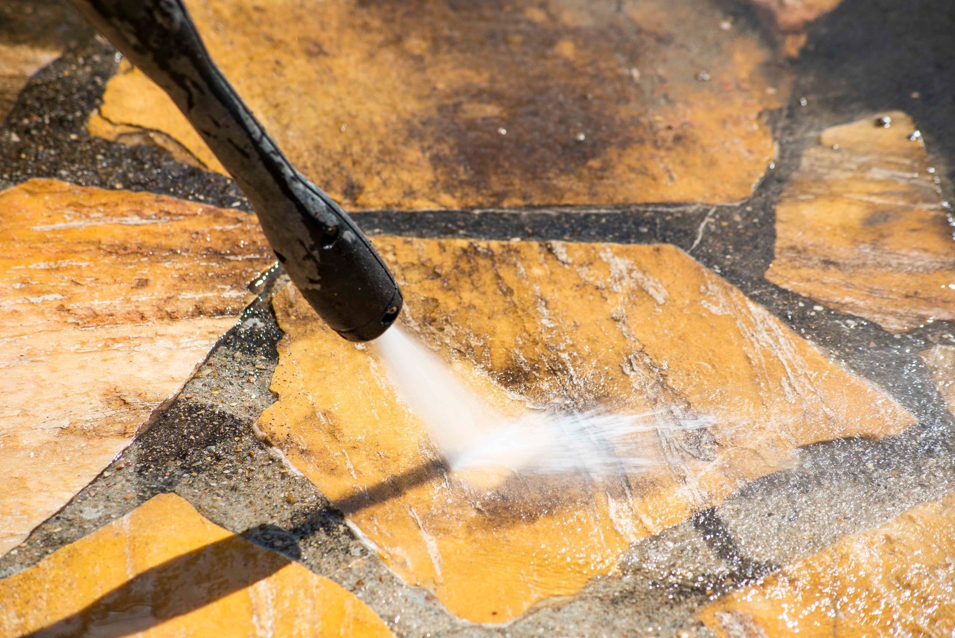 Un nettoyeur haute pression projette de l'eau sur le pavage en pierre jaune, nettoyant ainsi la surface.