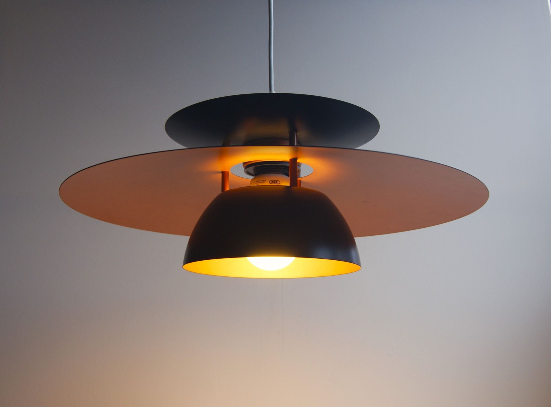 Suspension noire et orange avec une ampoule lumineuse sur un plafond gris.
