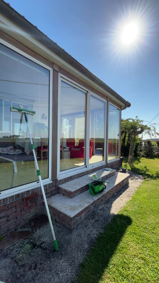 Patio ensoleillé avec de grandes baies vitrées, tuyau d'arrosage et pelouse verte à côté d'une maison moderne.