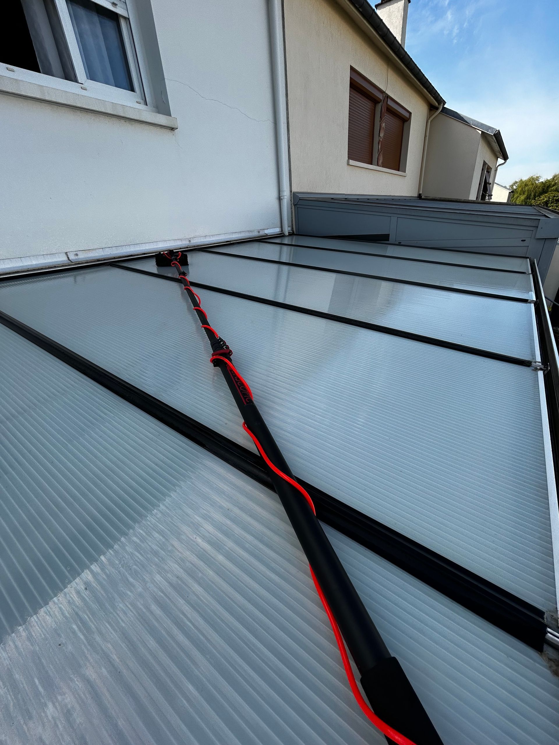 Gros plan sur un ensemble de panneaux solaires installés sur le toit d'une maison blanche, avec des sangles de sécurité rouges fixées aux panneaux.