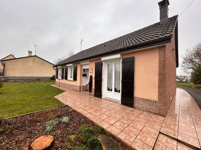 Maison de plain-pied couleur pêche avec terrasse carrelée et pelouse par temps couvert.